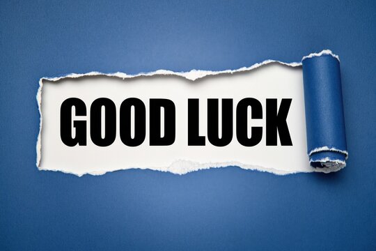 Good luck phrase written on white paper under torn dark blue background