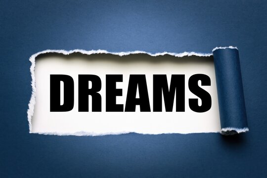 Dreams word written on white paper under torn dark blue background
