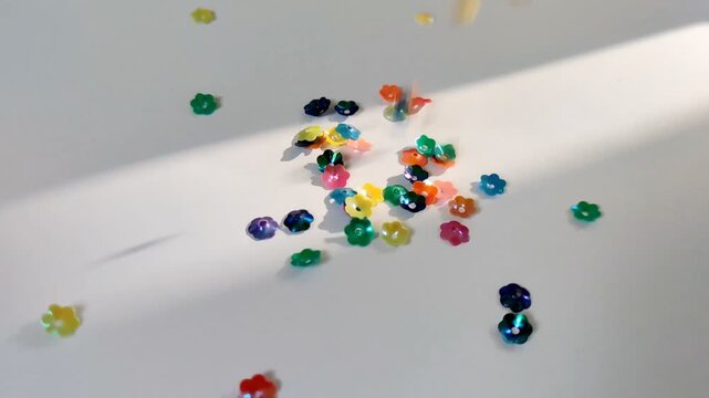 Slow Motion of Iridescent Flower Sequins Falling on Clean White Paper with Sunbeam Light