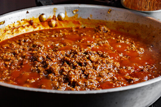 Bolognese meat sauce cooking in frying pan close-up photography of homemade bolognese sauce simmering inside a large aluminum frying pan. 