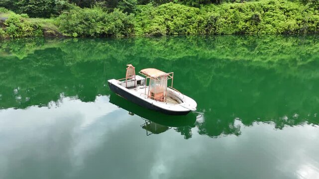 Drone aerial view of a small boat floating on crystal-clear emerald water in a flooded quarry surrounded by lush tropical rainforest near Crique Crabe, French Guiana.