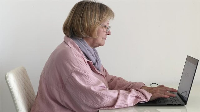 Senior Woman Handling Online Paperwork at Home. Senior woman using a laptop to read and manage online documents at home. Mature adult working with digital paperwork and computer tasks.
