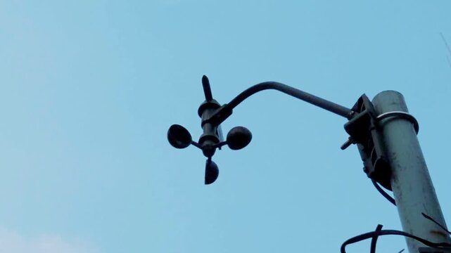 Low-angle shot of a digital cup anemometer spinning against a clear blue sky. 