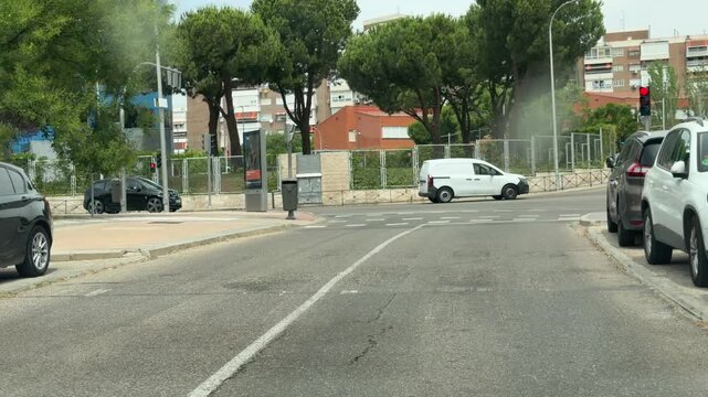 MADRID, SPAIN - June 24, 2026: Vehicle approaches a signalized urban intersection with parked cars, apartment buildings and city traffic. Residential neighborhood with modern office building and roads