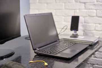 Fototapeta premium Black laptop on glossy desk with monitor, smartphone stand, and yellow ethernet cable