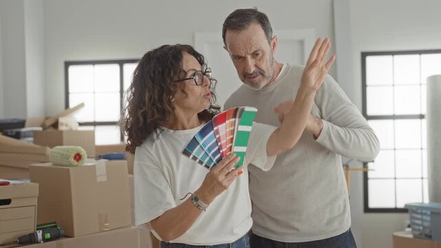 Woman holds paint swatches and points with hand at wall while man watches in building; renovation planning focused.