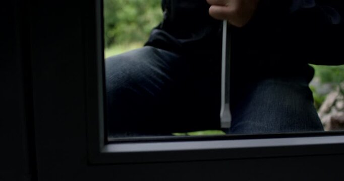 Close-up shot through a glass window pane of hands gripping a tool to pry the frame open