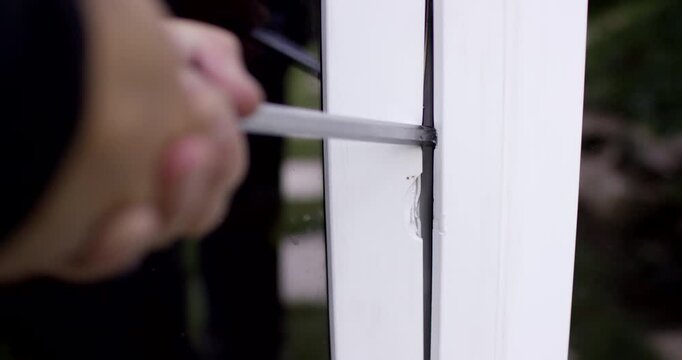 Close-up view from above of a hand using a tool to pry the edge of a white window frame