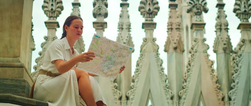 Woman reading map on steps of Duomo rooftop surrounded by spires in Milan, Italy