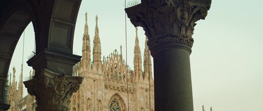 Milan Cathedral spires seen through decorated stone arch and column in gallery