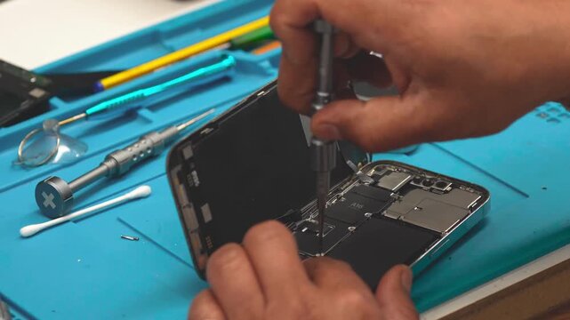 Technician repairing smartphone motherboard after disassembly in electronics repair workshop