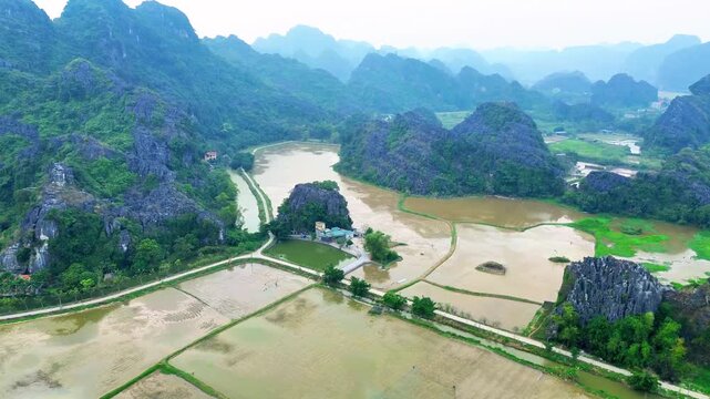 Aerial drone view of Tam Coc valley with green rice fields mountains and dramatic cloudy sky Vietnam