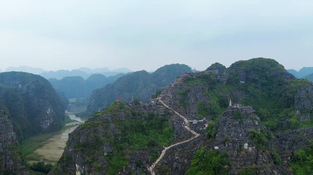Aerial drone view of mountain temple stairs overlooking rice fields and limestone mountains in Tam Coc Vietnam