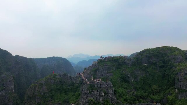 Aerial drone view of mountain temple stairs overlooking rice fields and limestone mountains in Tam Coc Vietnam