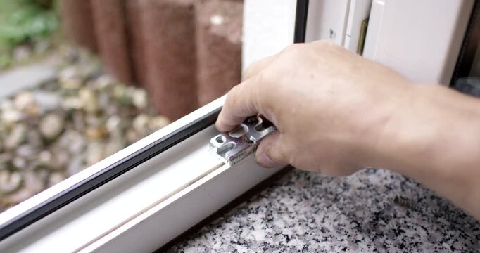 Close-up view of a hand test fitting a small metal lock mechanism on a white window frame track