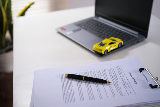 A yellow mini sports car model sits atop a laptop and documents on a desk, representing automotive price estimates, loan cost analysis, and budgeting concepts.
