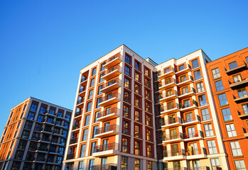 Fototapeta premium Facade of modern condominium in red and white colourful. Facade apartment building under blue sky. Modern facade building background. Balconies on blue sky. Modern residential facade 