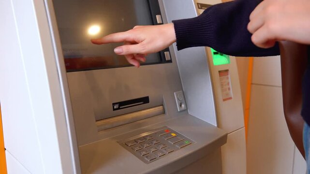 Close up view of a woman's hand inserting a bank card into an atm slot, entering her pin on the keypad, and navigating the on-screen menu to perform a financial transaction