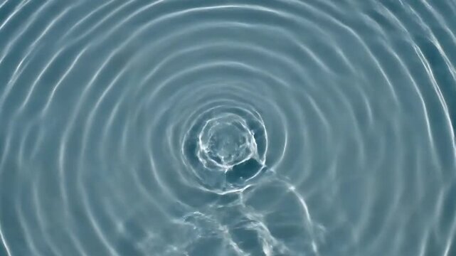 Close-up overhead view of concentric ripples spreading across a calm blue water surface with subtle light reflections Keywords: water, ripples, concentric, surface, liquid, wave, movement, pattern