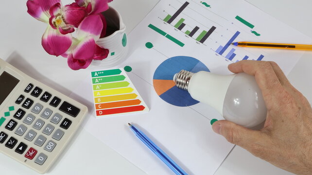 Scala di efficienza energetica con lampadina a LED, matita per i calcoli e modulo stampato che rappresenta il costo dell'energia.