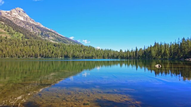 Calm waters of Bradley Lake perfectly mirror the rugged snowcapped Teton peaks above