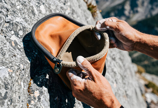 A climber's chalk-covered hands actively gripping and pulling open the stiff mycelium-leather rim of a bouldering chalk bag.