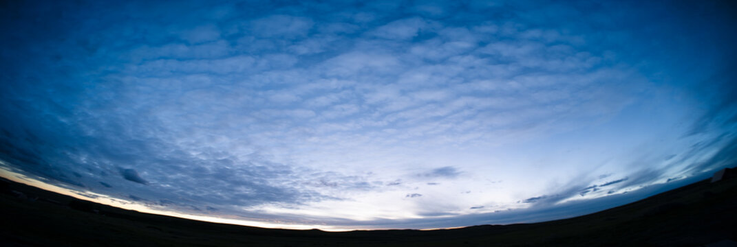 Fish-eye panorama of colorful blue evening clouds with silhouetted hills along the horizon.
