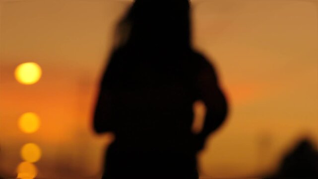 Silhouette of a woman jogging along a road at sunset with glowing street lights and dramatic orange sky, captured in slow motion for fitness, exercise, and healthy lifestyle concepts