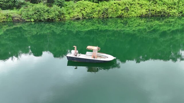 Aerial drone footage pulling away from a small boat floating on calm emerald water in a flooded quarry surrounded by tropical vegetation in French Guiana.