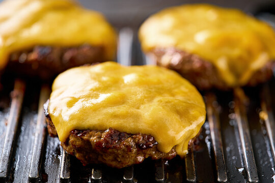 Melting cheese on a beef burger patties grilling a hot barbecue grill.