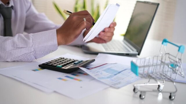 Checking purchase orders or invoices on a desk. A man sits at his desk holding invoices to calculate company expenses, analyze, and evaluate expenses.
