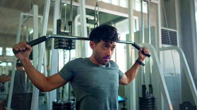 Athletic man performing a lat pulldown exercise on a strength training machine in a fitness center