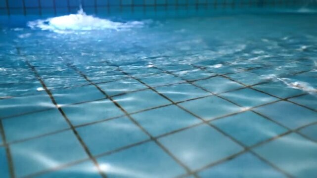 Underwater view of a swimming pool with blue tiles and rippling water surface