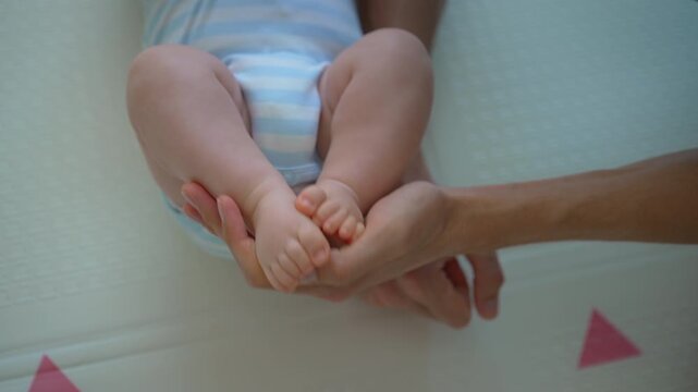 Father gently touching baby son's feet on floor. Close-up.