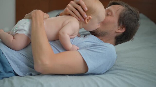 Smiling father holding his three month old baby son belly to belly on bed.