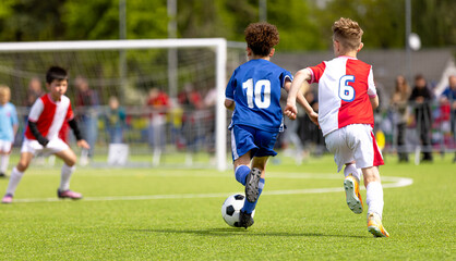 Naklejka premium Youth Soccer Tournament: Boys in Blue and Red Uniforms Racing for the Ball. Sports Competition For Kids