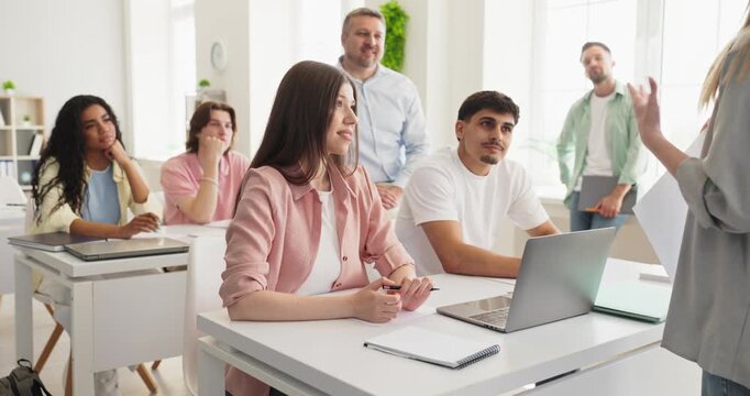 Teacher and students in classroom discussion lesson. Adult learners engage with the instructor in a bright room using laptops and notebooks. Concept of collaboration in modern education.