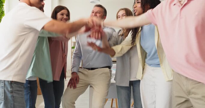 Team coworkers in huddle show unity and success. Diverse colleagues stack hands in a bright office, ready to collaborate, show teamwork with a leader, and achieve goals. We act as one team.