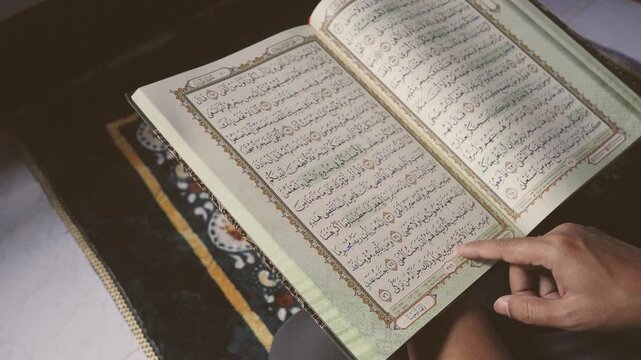 Close-up of a Muslim reading the Holy Quran on a prayer mat during quiet indoor worship. Islamic faith, spiritual reflection, sacred scripture study, religious devotion, and peaceful daily prayer conc