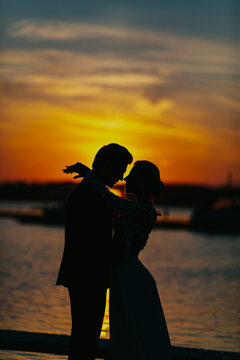 Romantic couple silhouette embracing at sunset by the water