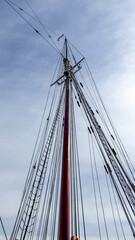 Fototapeta premium Tall ship mast reaches sky with many lines and poles at dock