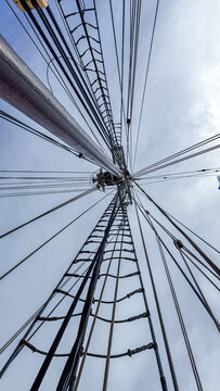 Looking up at the tall mast with many ropes on a sailing ship in the daytime