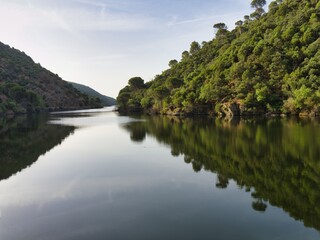 Fototapeta premium Beautiful lake surrounded by green hills in the afternoon sunlight with clear water reflecting trees and mountains