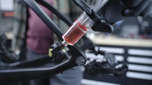 Close up video of a bicycle mechanic bleeding hydraulic brakes with mineral oil in a workshop. Professional bike maintenance process showing brake service, tools and technical repair work.