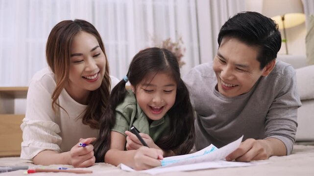Happy Asian Family Day Concept. Smiling father mother and daughter relaxing and painting on paper together in living room at home. Activity leisure of dad mom and child girl cheerful and fun to draw. 