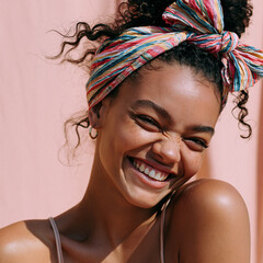 Naklejka premium young black woman smiling over shoulder with colorful headband, cheerful african woman with natural curly hair and playful smile, confident young woman wearing striped headband and gold hoop earrings