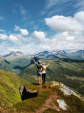 Couple in love hiking together friends travel in Norway boyfriend and girlfriend on the top cliff edge happy raised hands enjoy mountains views, active healthy lifestyle summer vacations trip outdoors