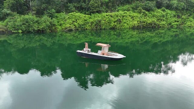 Smooth cinematic drone orbit around a small boat floating on emerald green water inside a flooded quarry surrounded by rainforest near Crique Crabe, French Guiana.