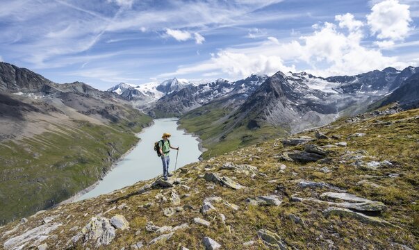 Mountaineer on the summit of Mont de la Blana, view of a blue mountain lake, Lac des Dix reservoir, behind mountain peak Mont Blanc de Cheilon with glacier, H&eacute;rm&eacute;nence, Valais Alps, Valais, Switzerland