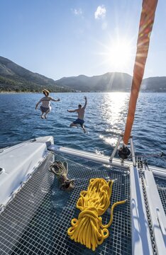 Young woman and young man jumping into the water, ropes on a sailing catamaran, Sun Star, sailing trip, Tilos, Dodecanese, Greece